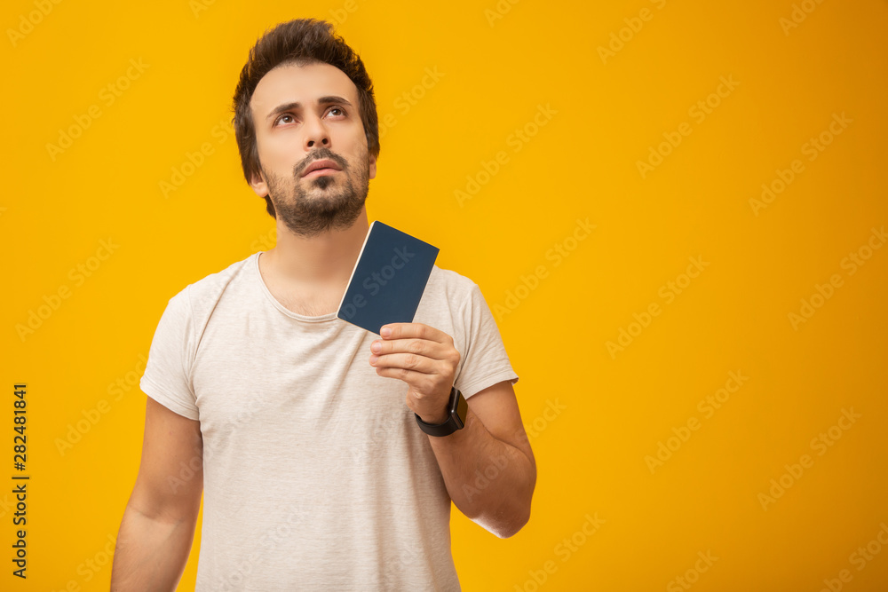 Young man holding a passport, work card or document, thinking. On yellow background Young man holding a passport, work card or document, thinking. On yellow background