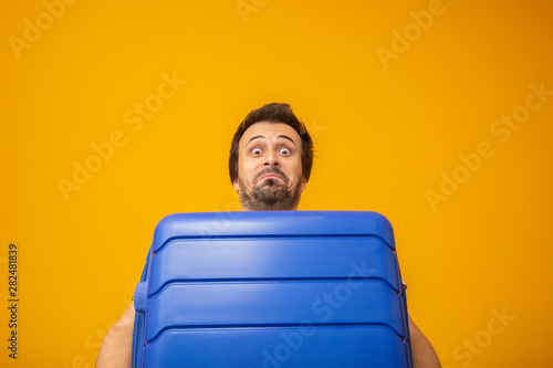 Funny man holding a heavy travel bag. On yellow background