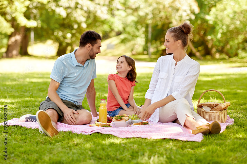 family, leisure and people concept - happy mother, father and daughter having picnic at summer park family, leisure and people concept - happy mother, father and daughter having picnic at summer park