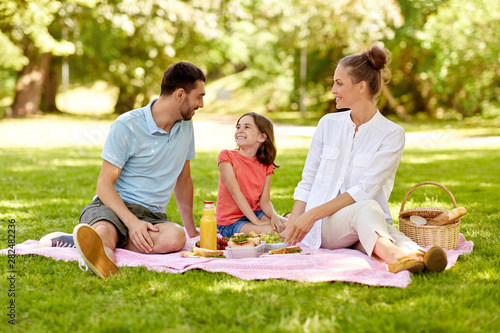 family, leisure and people concept - happy mother, father and daughter having picnic at summer park © Syda Productions