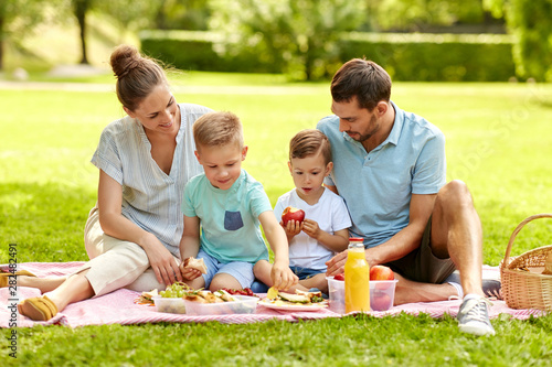 family, leisure and people concept - happy mother, father and two little sons having picnic at summer park