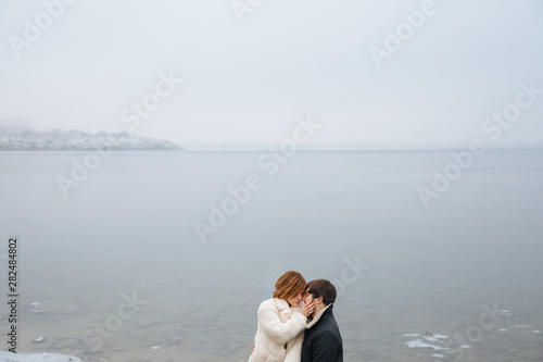 A couple in coats hugging on the banks of a frozen river photo