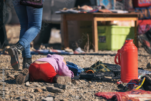 Obraz na płótnie Pristine Mongolia. Mongolian Boy In Red Pants Sleeping On Stones Among Passing People During The Golden Eagle Hunters Festival. Happy Childhood. Red Thermos w salonie