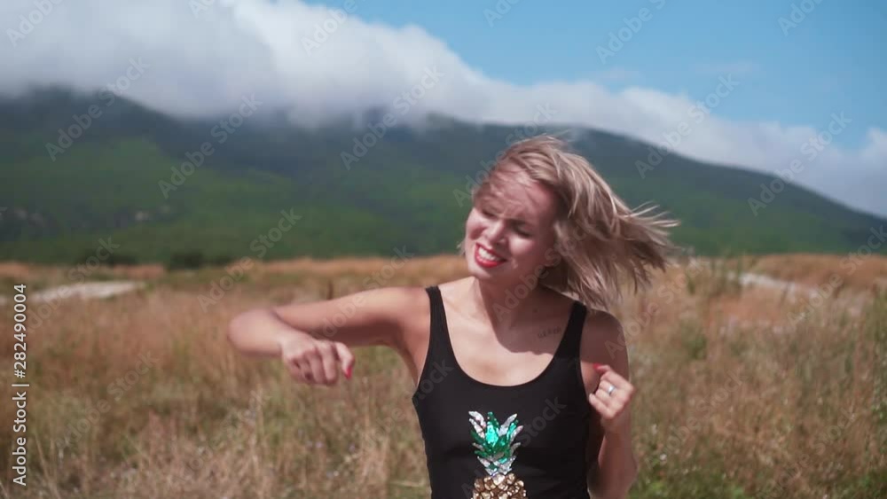 Sexy girl dancing on a road in the mountains on a sunny day, sunbeam. The blonde girl has fun and funny dancing in an open bathing suit on a background of mountains in nature. Close-up. Sexy girl dancing on a road in the mountains on a sunny day, sunbeam. The blonde girl has fun and funny dancing in an open bathing suit on a background of mountains in nature. Close-up.