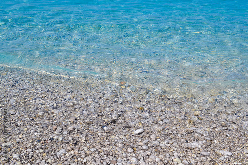 square background image of calm turquoise sea on shingle beach