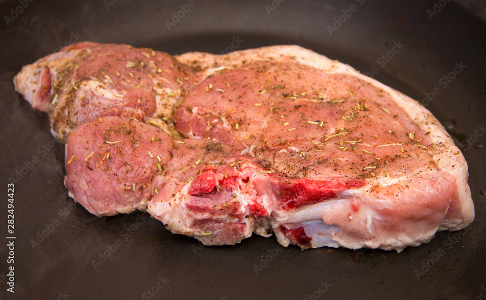 Fresh raw pork steak with spices roasting on frying pan Fresh raw pork steak with spices roasting on frying pan