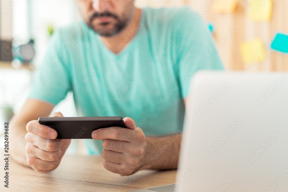 Freelancer playing mobile video game on smartphone in home office Freelancer playing mobile video game on smartphone in home office