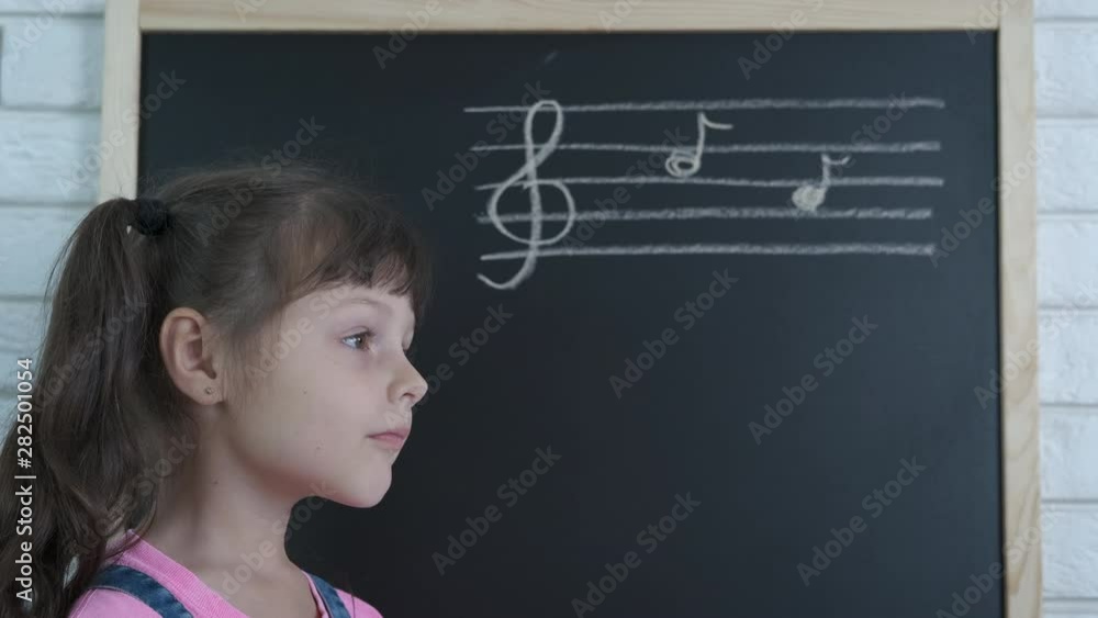 Little girl at a music lesson. Cute little girl at the school blackboard with written musical notes. Little girl at a music lesson. Cute little girl at the school blackboard with written musical notes.