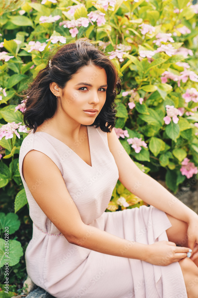 Outdoor portrait of beautiful young woman with professional makeup and hair styling, green natural background with pink hydrangea flowers Outdoor portrait of beautiful young woman with professional makeup and hair styling, green natural background with pink hydrangea flowers