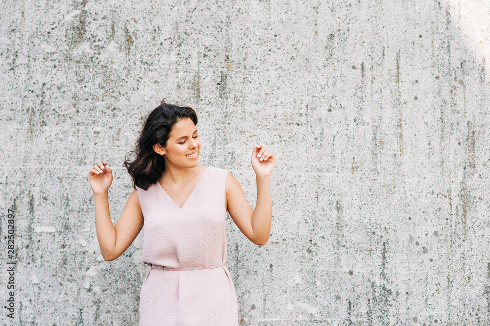 Urban fashion portrait of beautiful young woman posing on gray wall background, arms up Urban fashion portrait of beautiful young woman posing on gray wall background, arms up