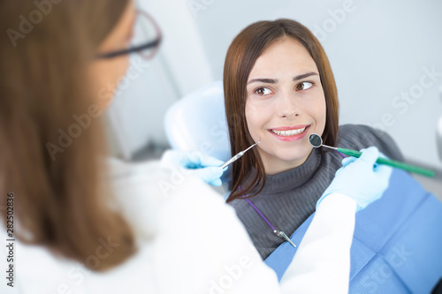 A smiling girl sitting in a dental chair is examined by a doctor. Young woman with white and healthy teeth.