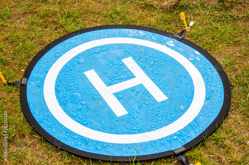 Blue landing place for drone with drops of water. The Landing Parking Pad take off platform for copter is used in high lawn and dusty ground in order to deface the spoilage of a high priced aircraft