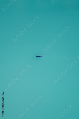 Vertical photography of a lone boat sailing at turquoise Oeschinensee in Switzerland. Swiss Oeschinen Lake. Aerial view, blurred boat. Minimalist nature. Escape, lost. Concept, abstract