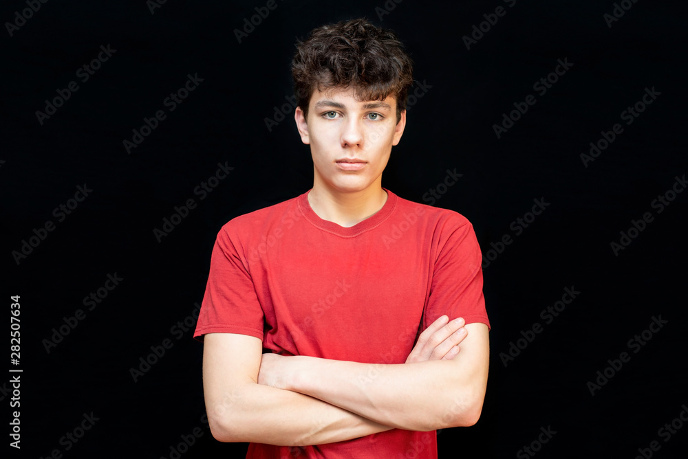 Portrait of a handsome teenage boy in a red T-shirt on a dark background. The guy has dark curly hair Portrait of a handsome teenage boy in a red T-shirt on a dark background. The guy has dark curly hair