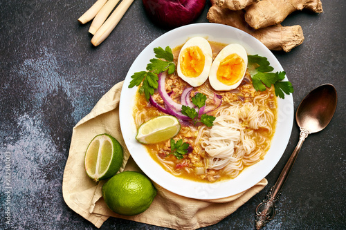 Mohinga at dark background in white plate. Mohinga is a burmese cuisine fish soup with catfish, rice noodles, chicken eggs and lime.