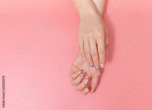Tender hands with perfect nude manicure on trendy pastel pink background. Place for text