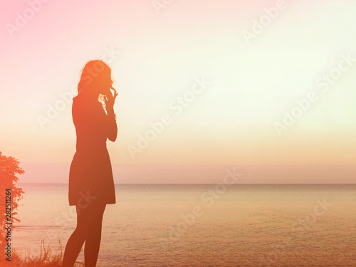 Silhouette of a young woman who stands on a rock in the sea and looks at the sunset. Focus on the girl © Aliaksandr Kisel