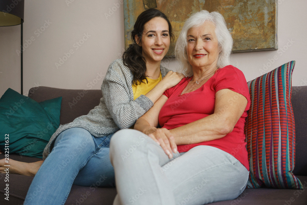 Portrait smiling senior mother sitting with daughter on living room sofa Portrait smiling senior mother sitting with daughter on living room sofa