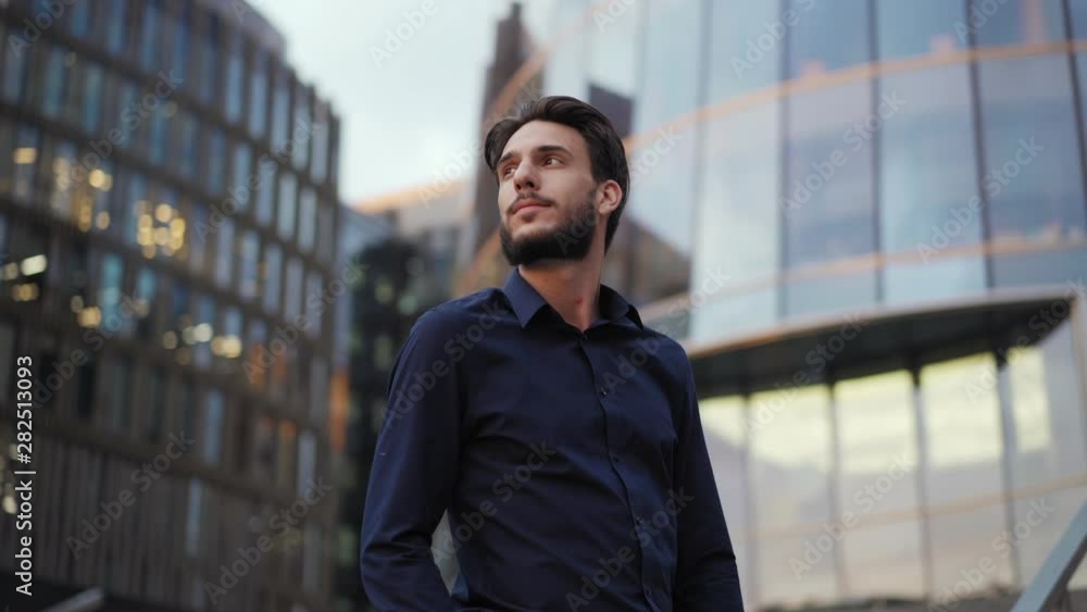 Camera approaching handsome young businessman standing on steps of modern office building with hand in pocket, drinking takeaway coffee, looking away and contemplating Camera approaching handsome young businessman standing on steps of modern office building with hand in pocket, drinking takeaway coffee, looking away and contemplating