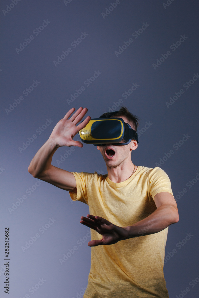 technology, gaming, entertainment and people concept - young man with virtual reality headset or 3d glasses. Studio shot, gray background. technology, gaming, entertainment and people concept - young man with virtual reality headset or 3d glasses. Studio shot, gray background.