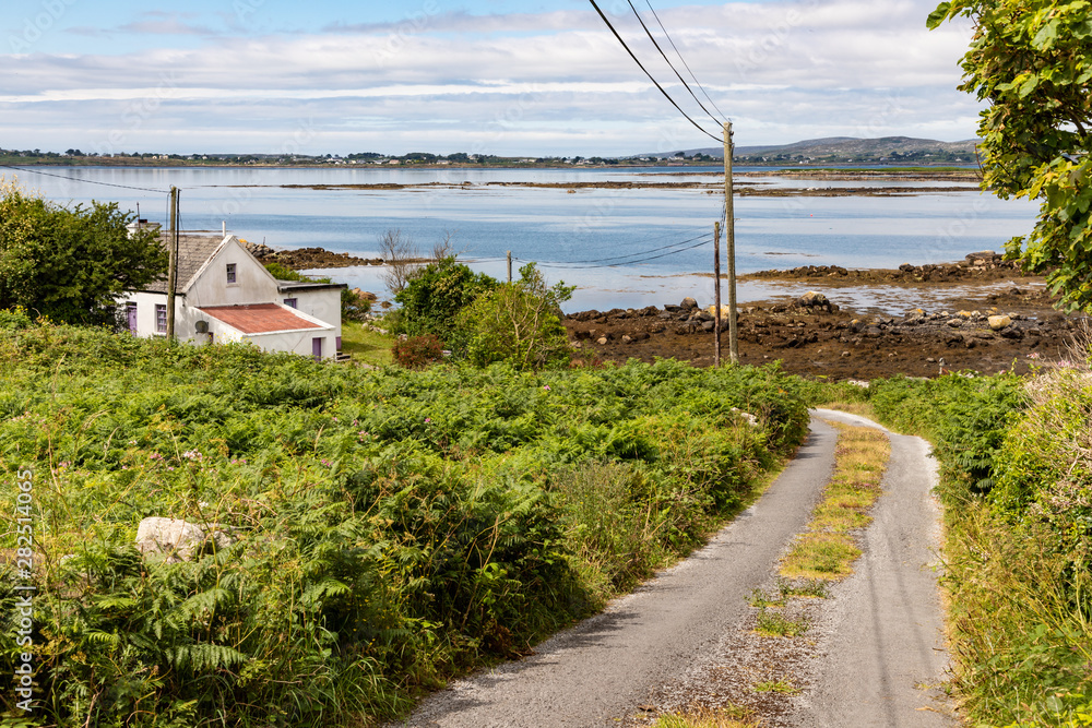 Small road and house with bay in background in Carraroe