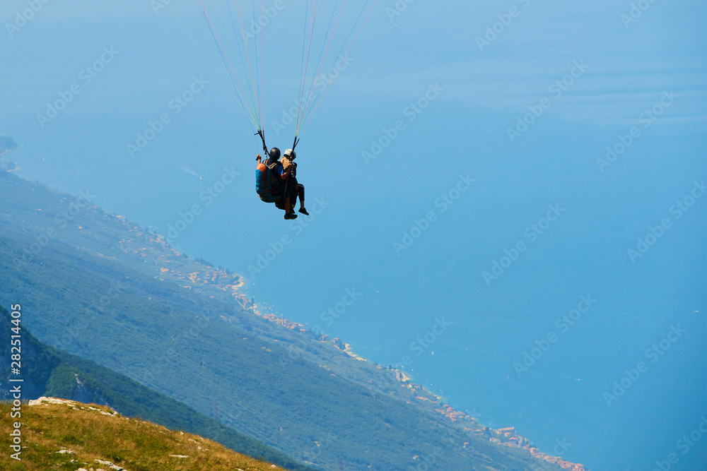 Paraglider flying over the Garda Lake (Lago di Garda or Lago Benaco). Paragliding on Monte Baldo. Panorama of the gorgeous Garda lake surrounded by mountains, Malcesine, Italy Paraglider flying over the Garda Lake (Lago di Garda or Lago Benaco). Paragliding on Monte Baldo. Panorama of the gorgeous Garda lake surrounded by mountains, Malcesine, Italy
