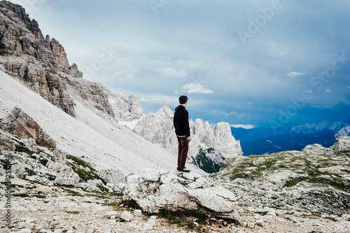 Teenage boy standing on rock overlooking rugged mountains, Drei Zinnen Nature Park, South Tyrol photo