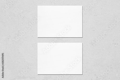 Two empty white horizontal rectangle a5 sized card mockups with soft shadows on neutral light grey concrete wall background. Flat lay, top view