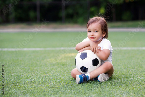 Portrait of sad unhappy boy sitting on football field and holding with both hands or embracing soccer ball. May be his team lost or he wanted to play but was rejected. Competition emotions concept © AMR Studio