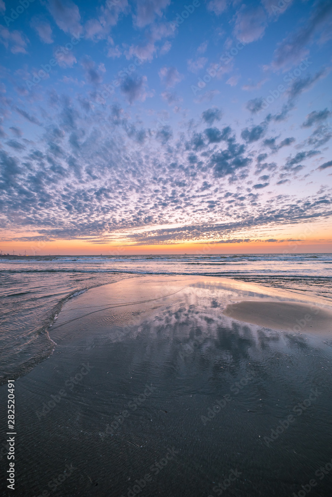 Fototapeta premium Colorful sunset at the dutch beach with beautiful reflections of the clouds in wet sand