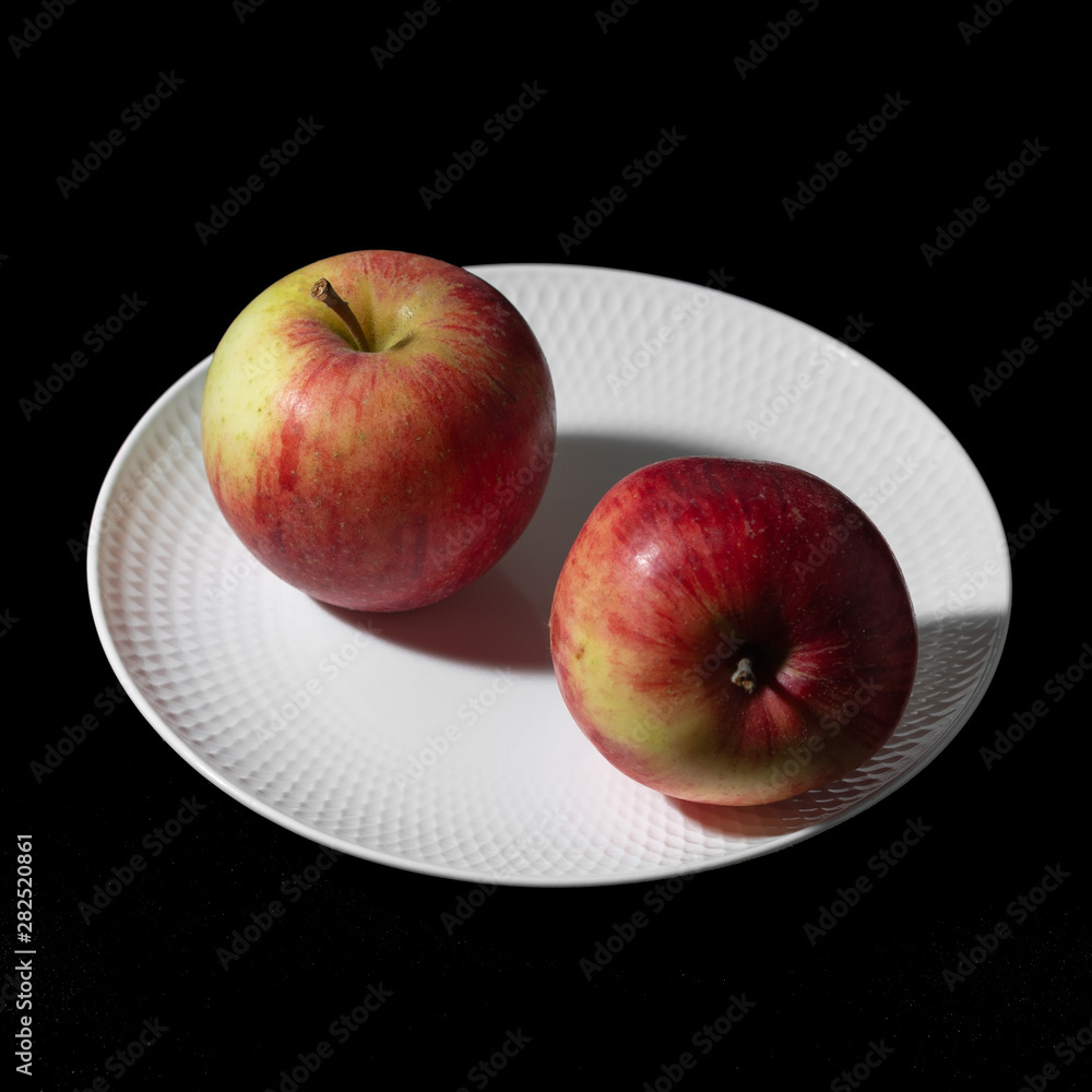 Two apples lie on a white plate on a black background close-up Two apples lie on a white plate on a black background close-up