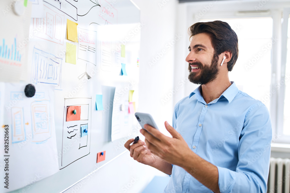 Businessman standing in front of a whiteboard and using his smartphone Businessman standing in front of a whiteboard and using his smartphone