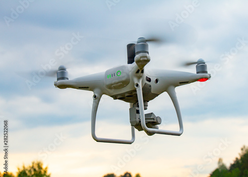 UAV White drone Quadr copter in flight with geodesic module and digital camera explores the area on the background of a sunset with clouds. The copter in the air take aerial photo in the blue sky