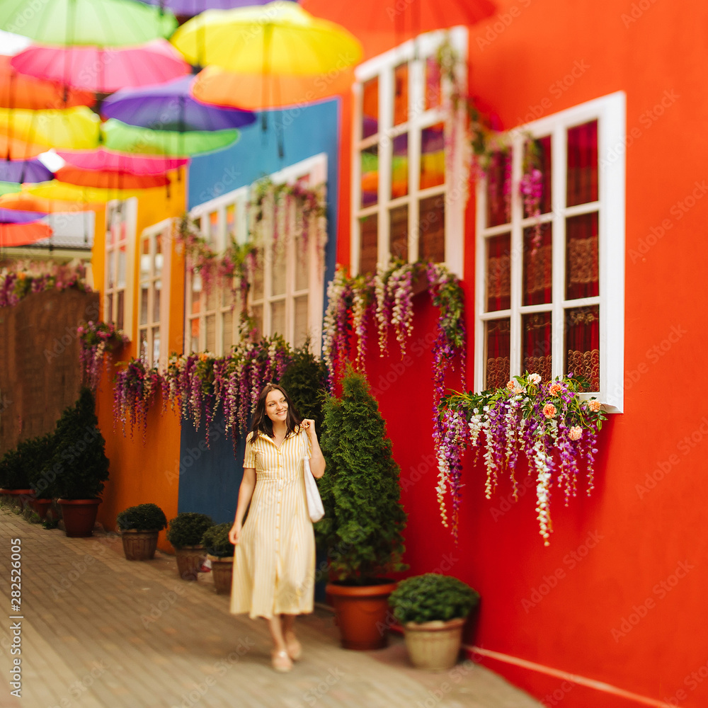 Fototapeta premium Travel tourist brunette woman in yellow dress walks the streets with bright decoration of the city. Tilt-shift lens blur