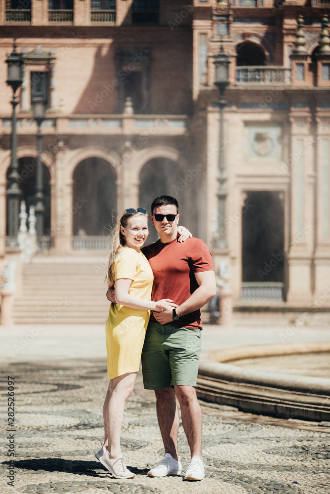 Traveling young couple walking around old city centre. Beautiful tourist visiting historic city on holiday. Man and woman cuddling and enjoying trip in Portugal. Sweet pair posing near fountain Traveling young couple walking around old city centre. Beautiful tourist visiting historic city on holiday. Man and woman cuddling and enjoying trip in Portugal. Sweet pair posing near fountain