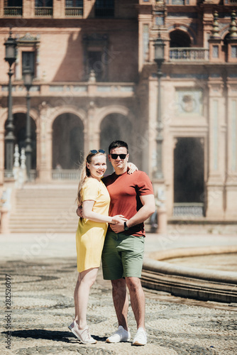 Traveling young couple walking around old city centre. Beautiful tourist visiting historic city on holiday. Man and woman cuddling and enjoying trip in Portugal. Sweet pair posing near fountain