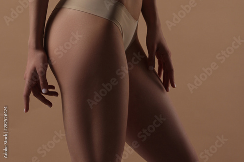 Thin young woman in underwear on beige background