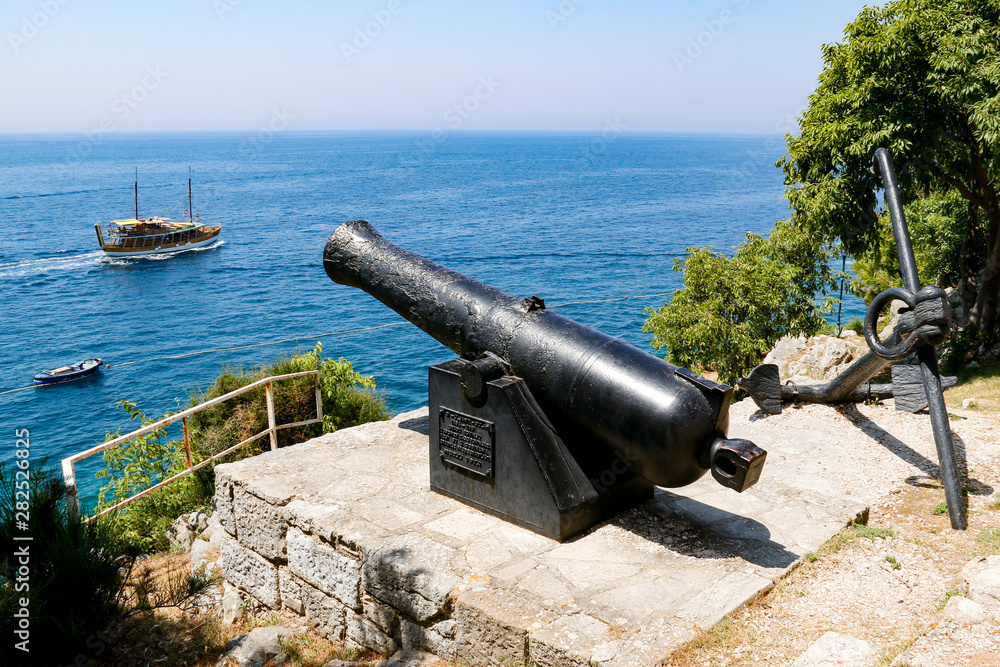 Old cannon in Rovinj, Croatia pointing towards passing cruise boat