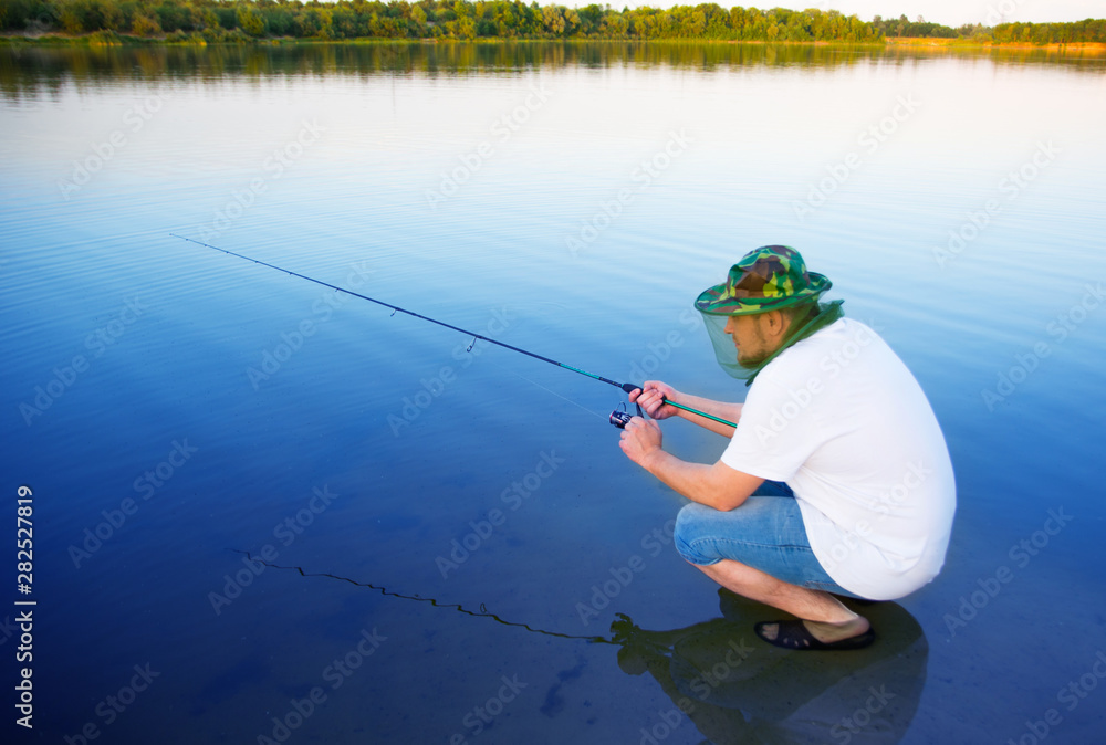 man catches a fish spinning on the background of water in the summer. Russian fishing man catches a fish spinning on the background of water in the summer. Russian fishing