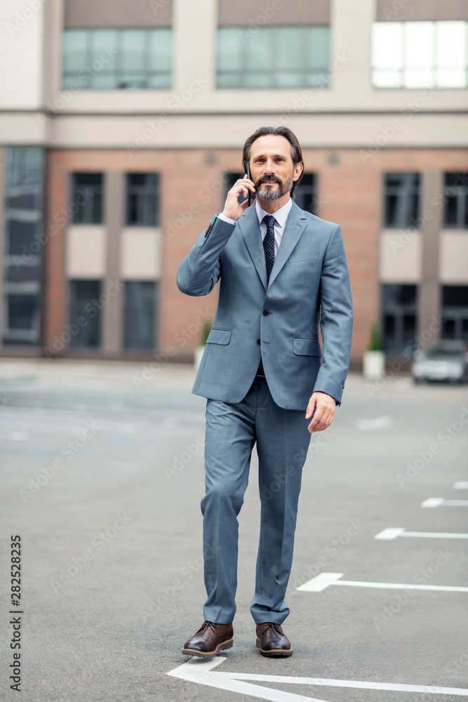Man wearing grey suit calling colleague while walking by foot Man wearing grey suit calling colleague while walking by foot