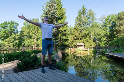 A young man meets the dawn, standing in front of a pond with arms wide apart and turning his face to the sky