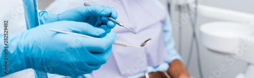 panoramic shot of dentist in blue latex gloves holding dental instruments