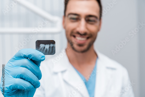 selective focus of x-ray in hand of cheerful dentist in dental clinic