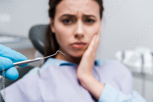 selective focus of dentist in latex glove holding dental instrument near woman having toothache