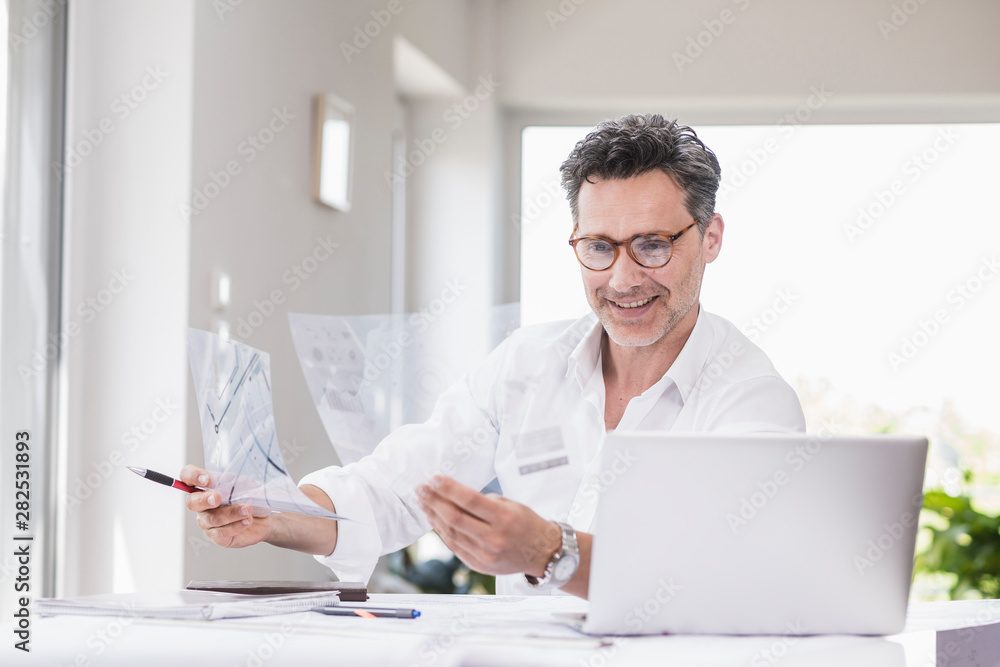 Architect preparing presentation, sitting in office looking at foil plan Architect preparing presentation, sitting in office looking at foil plan