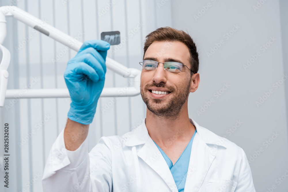 selective focus of cheerful dentist in glasses holding x-ray in clinic selective focus of cheerful dentist in glasses holding x-ray in clinic