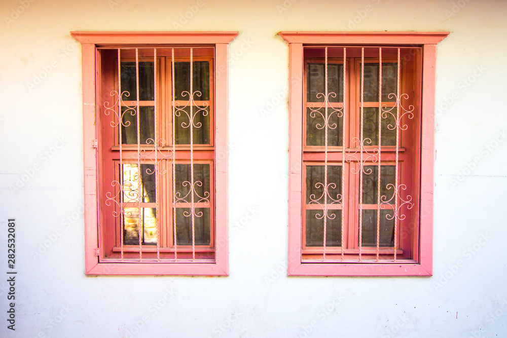 Fototapeta premium Antique windows in a pink hue. Protective metal bars are installed on the windows.