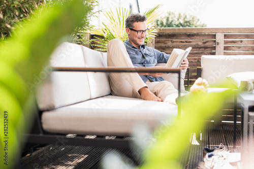 Confident man relaxing on the terrace, reading book photo