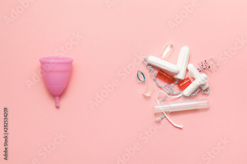 Reusable silicone menstrual cup and heap of tampons trash comparison on a soft pink background. Modern female intimate alternative gynecological hygiene. Eco zero waste concept photo