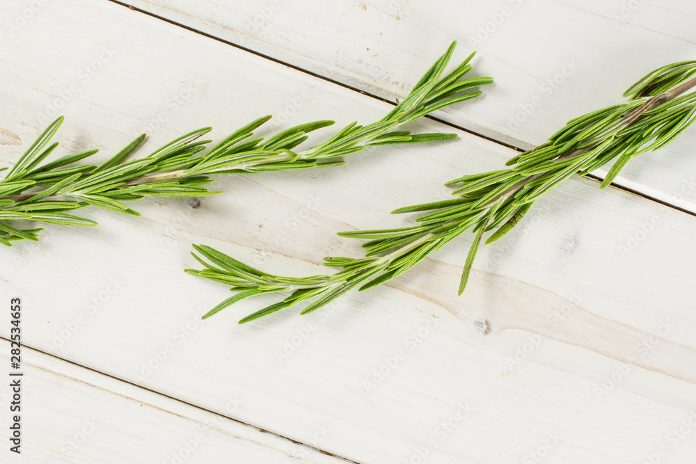 Group of two whole fresh evergreen sprig of rosemary needle leaves flatlay on white wood Group of two whole fresh evergreen sprig of rosemary needle leaves flatlay on white wood